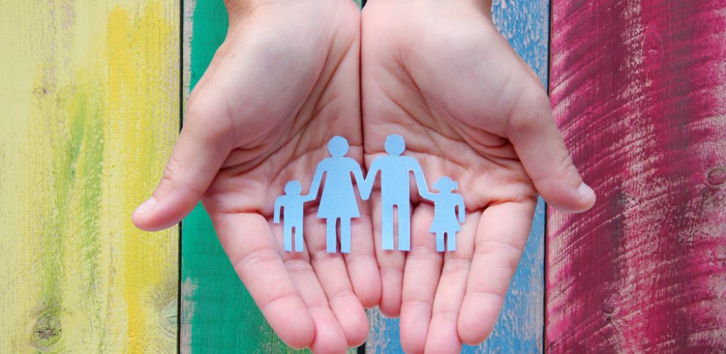 Paper,Family,In,Hands,On,Wooden,Coloured,Background,Welfare,Concept
