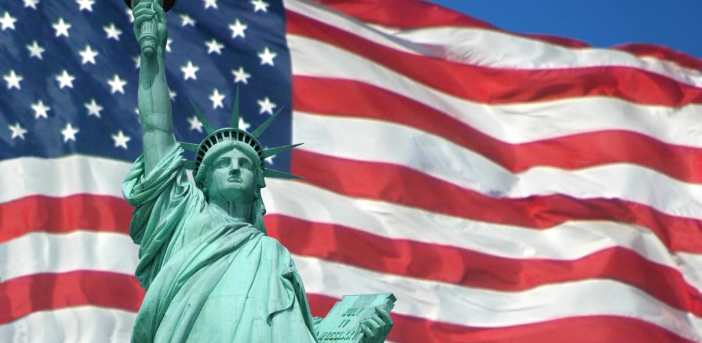Statue,Of,Liberty,With,The,U.s.,Flag,In,The,Background.